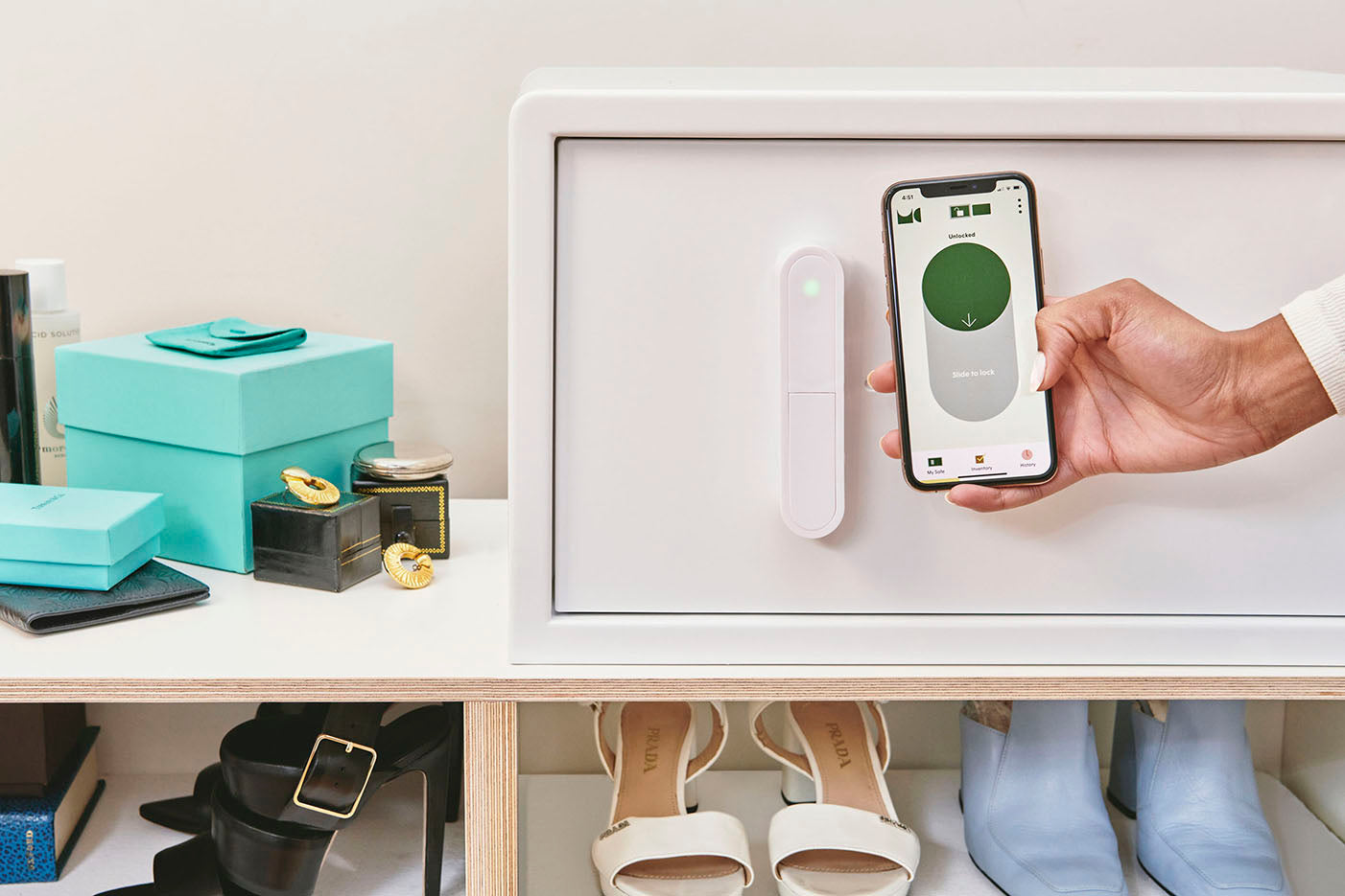 A white iCube sitting on top of a shelf with a hand holding a phone to show the iCube app. On the screen, the app is prompting them to slide to lock the safe.