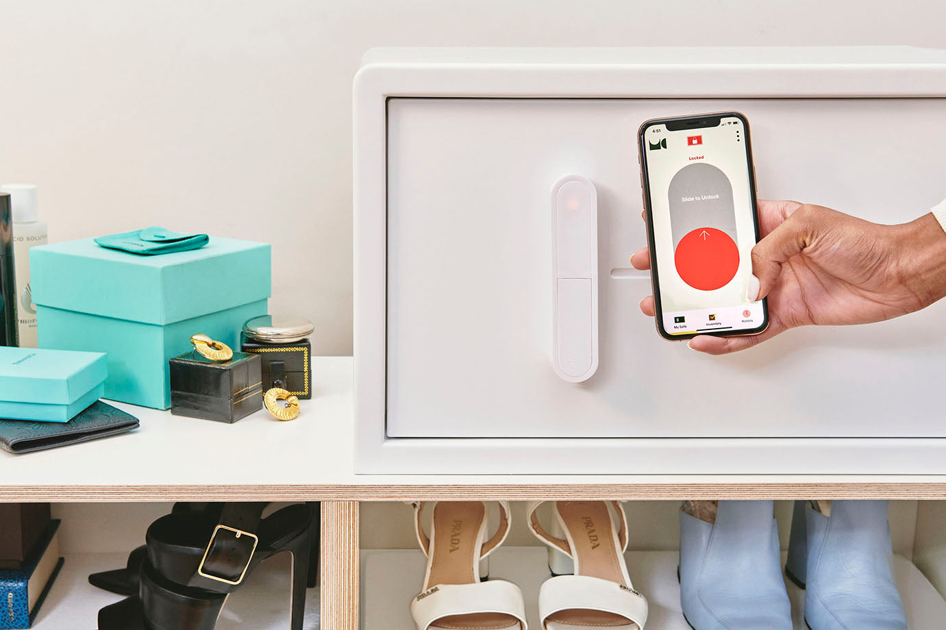 A white iCube sitting on top of a shelf with a hand holding a phone to show the iCube app. On the screen, the app is prompting them to slide to unlock the safe.
