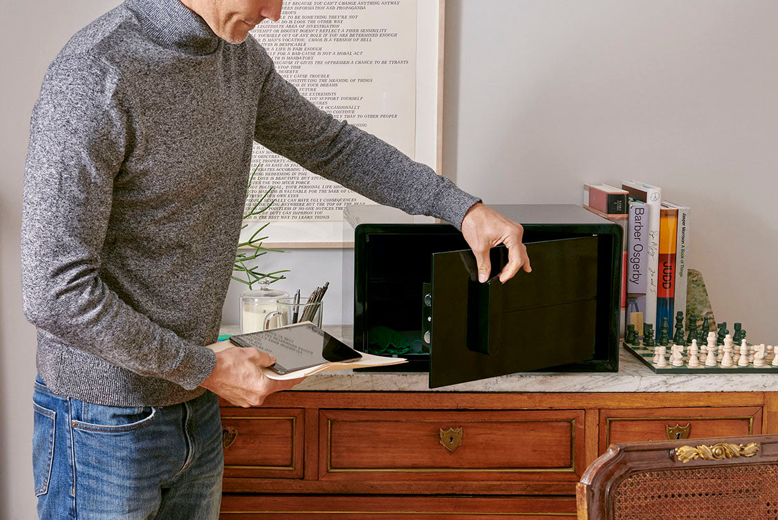 A black iCube sitting on top of a chest of drawers with a person opening the safe to put documents within the safe