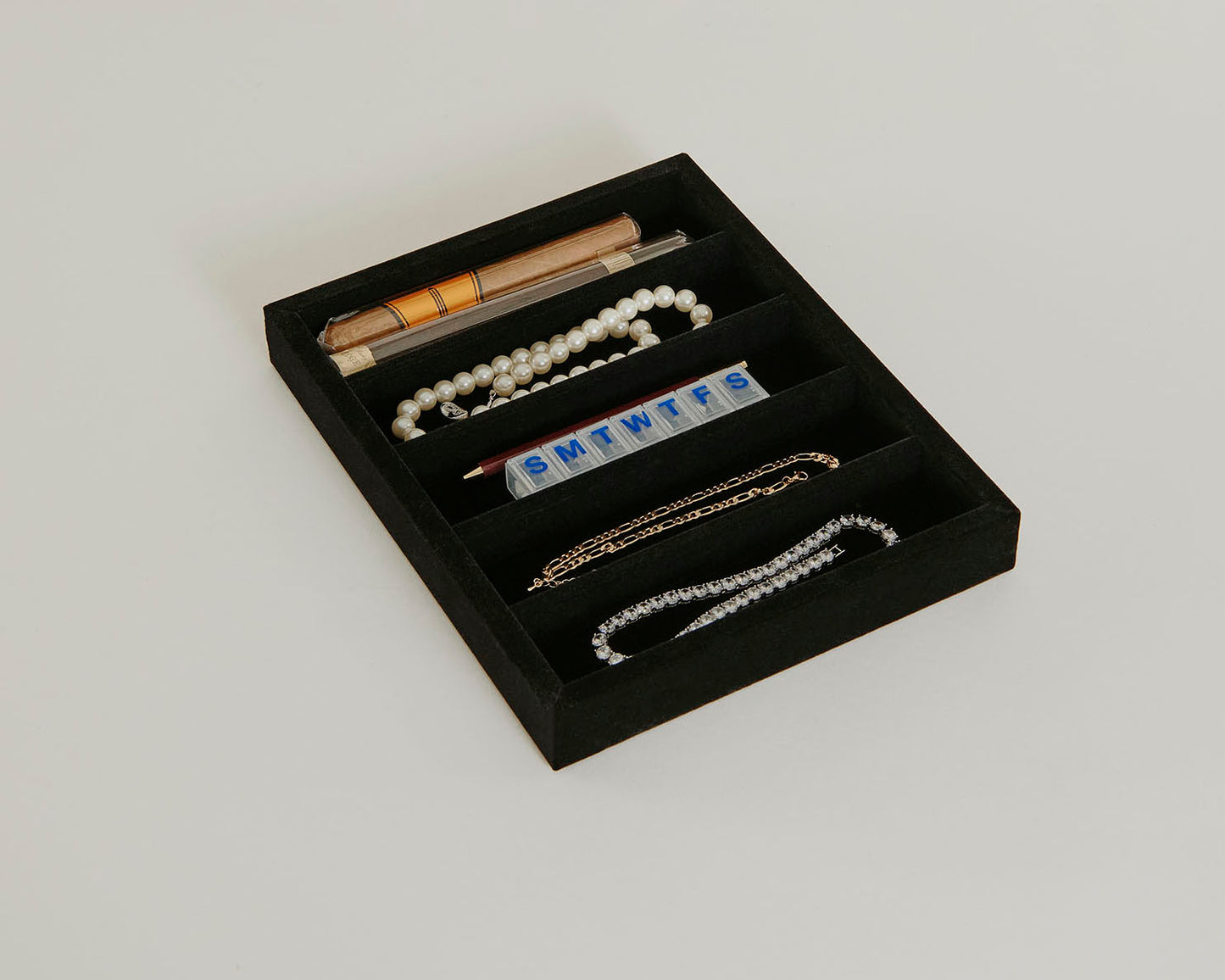 A black 6V tray with jewelry, medicine, and a cigar sitting within the tray