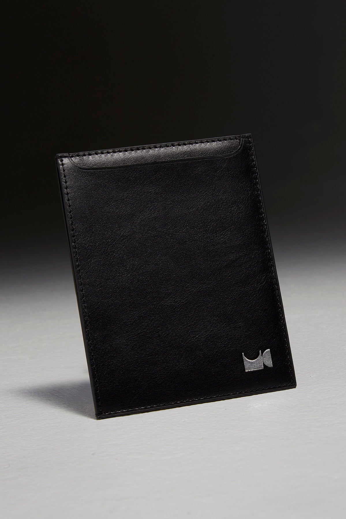 Black leather passport holder sitting in front of black backdrop